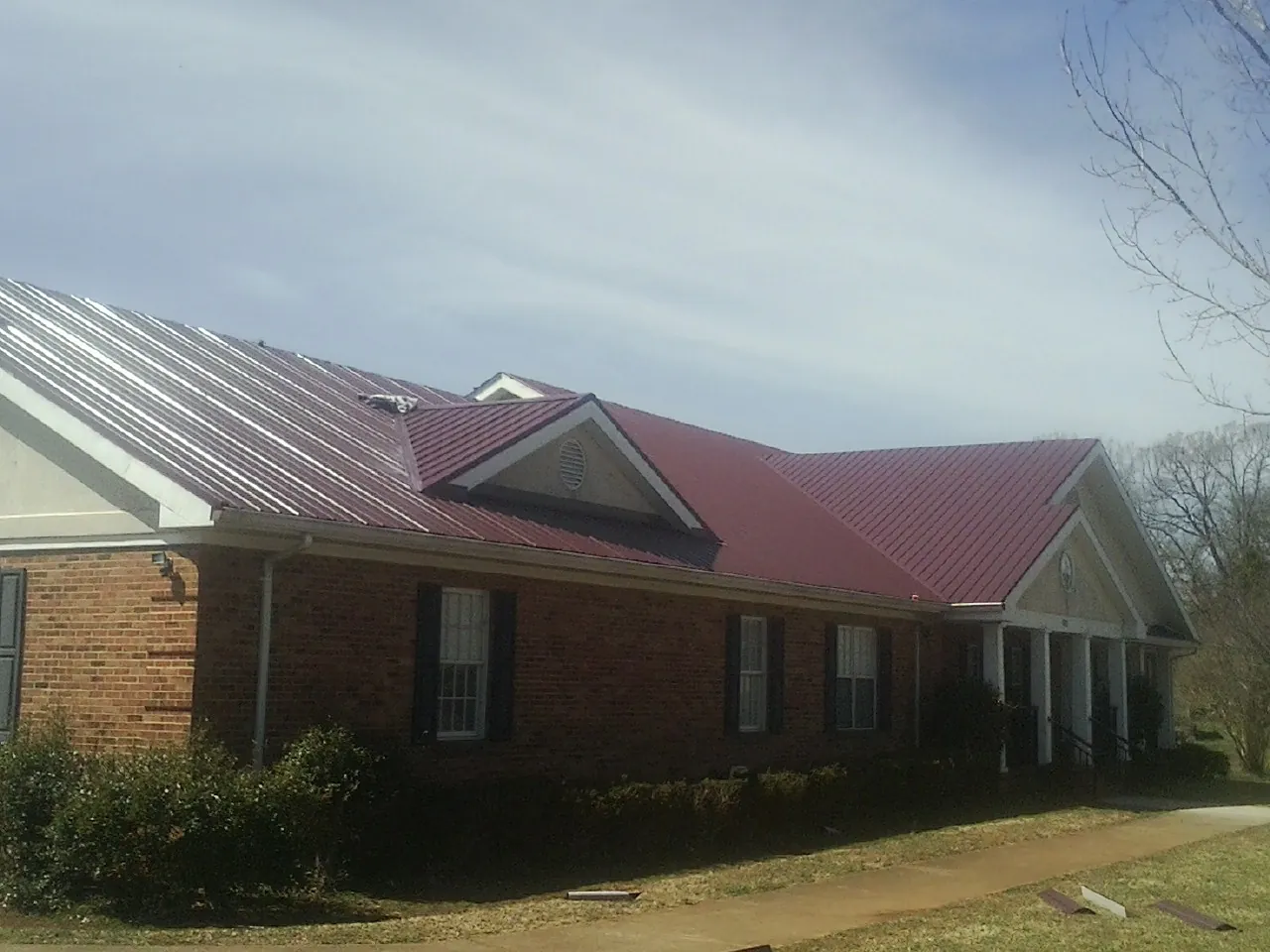 Red metal roof with gabled entries on a long brick building, from a Hail Damage Roof Repair job in Great Cacapon