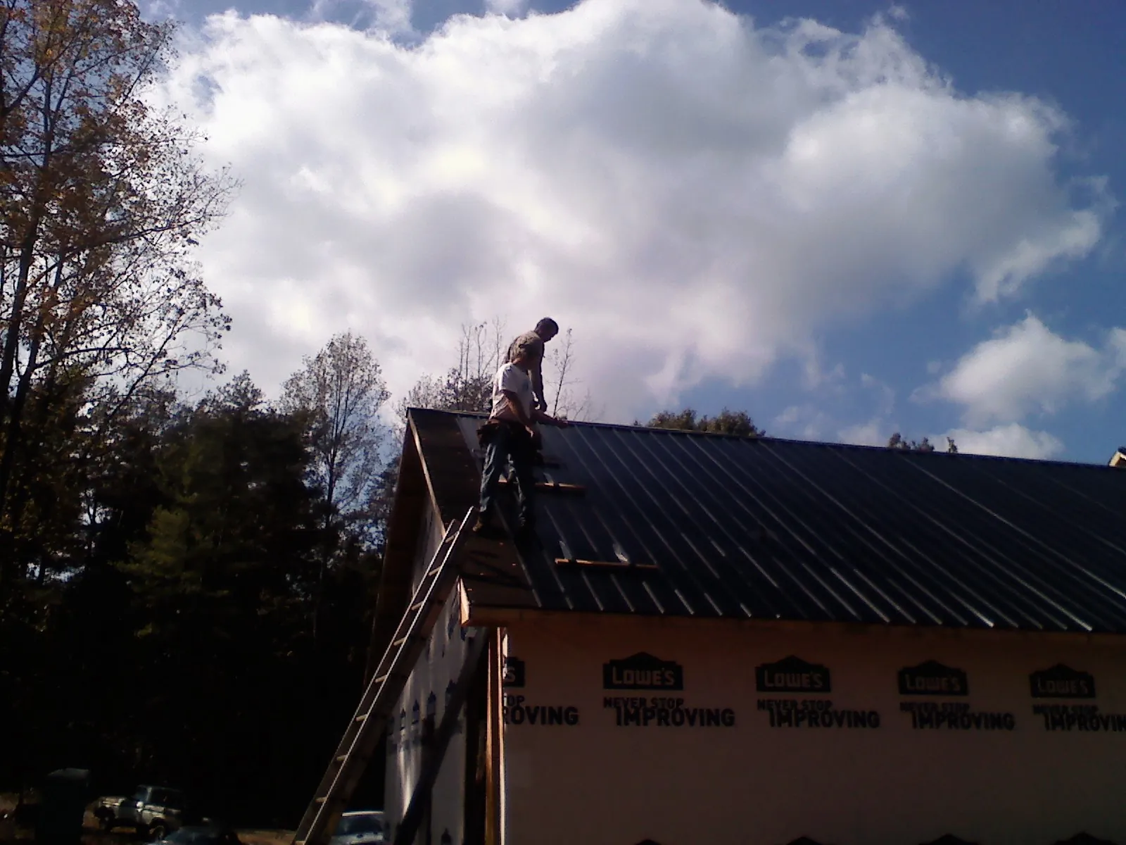 Roofer fastening dark metal panels high against a cloudy sky, from a Roof Inspection job in Great Cacapon