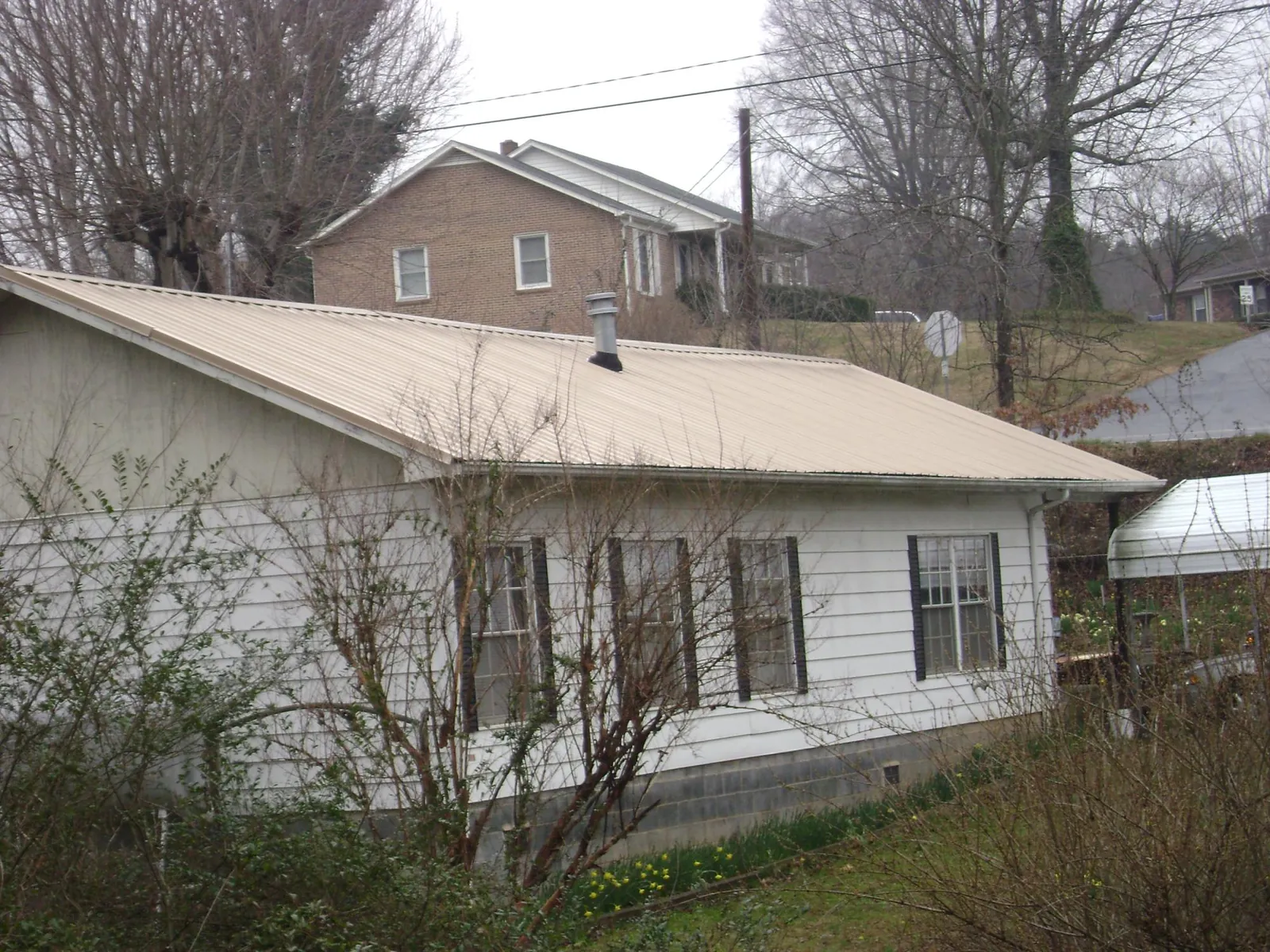 Tan metal roof on a white sided house set into a hillside — Commercial Roofing by Roofing Brothers in Great Cacapon